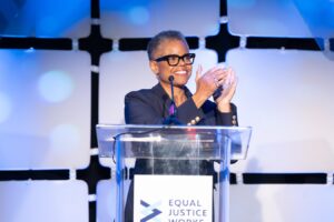 Photo of Verna Williams stood at a podium while she shares her 2024