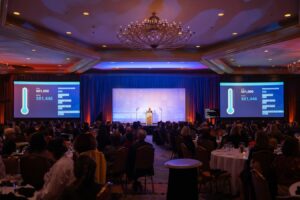 Wide shot of the 2025 Scales of Justice room at the Omni Shoreham Hotel, Screens show that the goal of $81k raised in one night has been met!