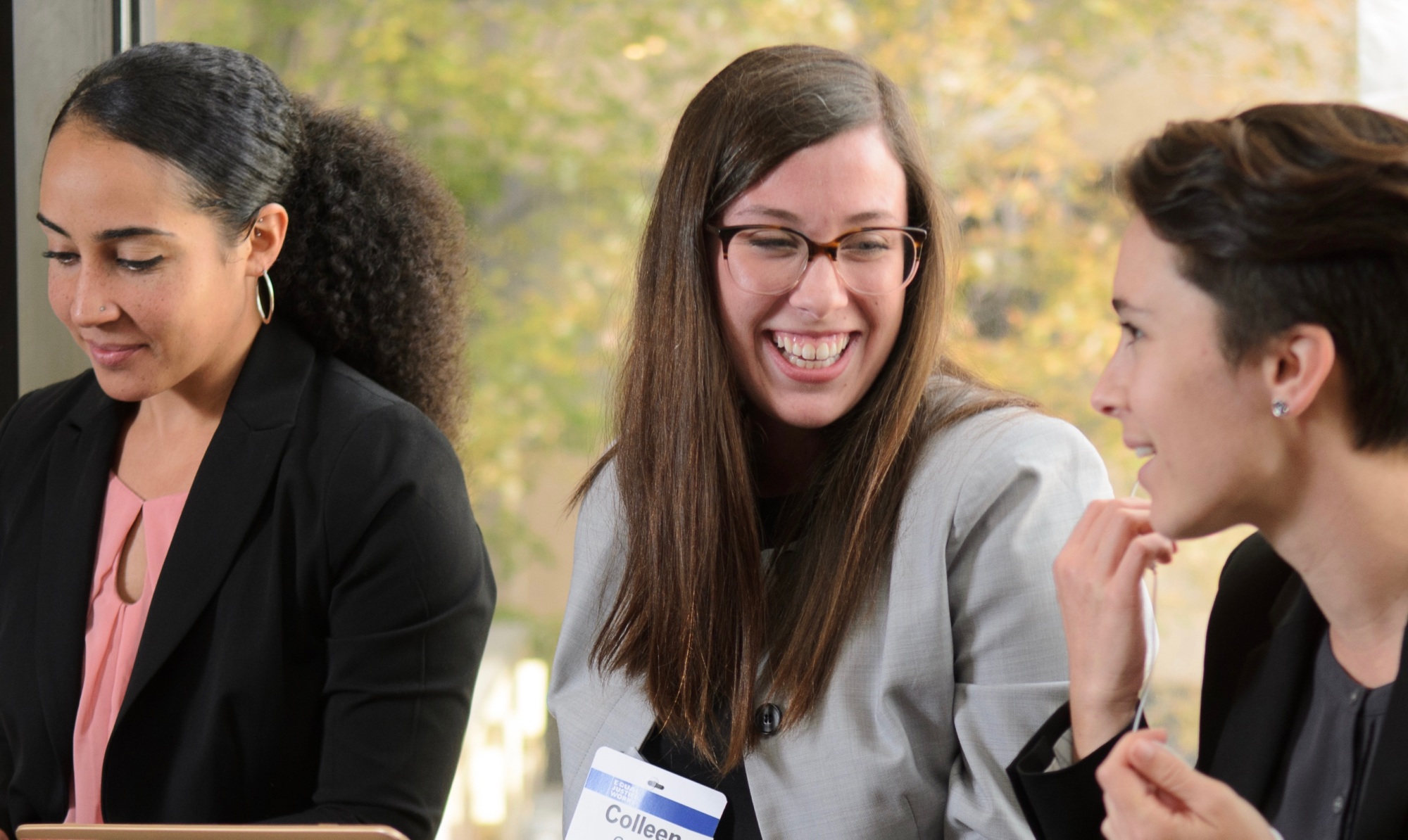 Three professional women sit and smile while looking at laptops