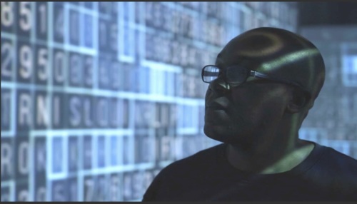 Silhouette of Clarence Okoh against blue tinted wall of blurred images