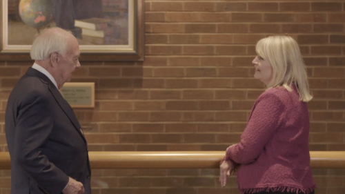 Bob Stein stands on the left and Laura Stein stands on the right smiling at each other