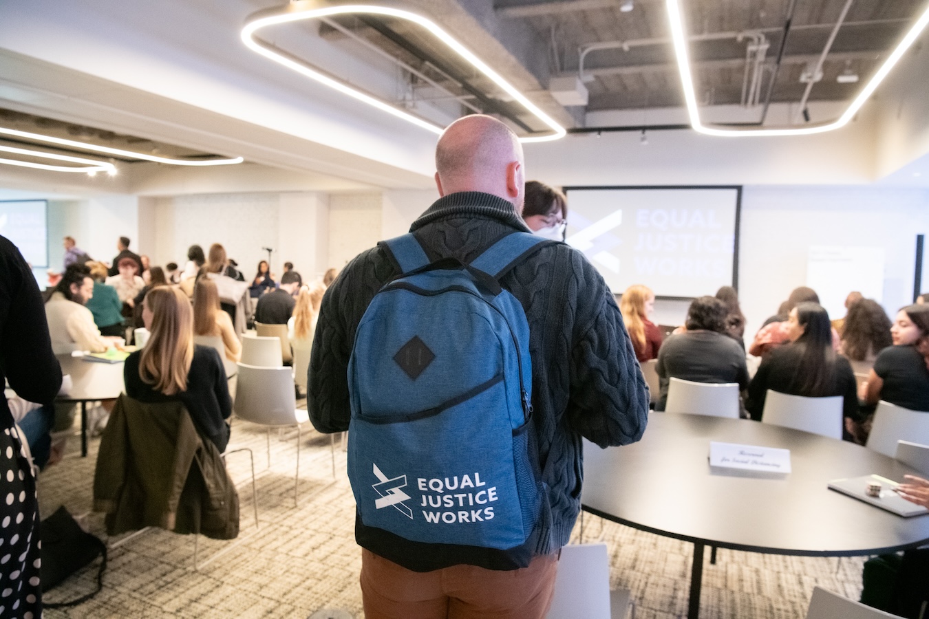 A Fellow walks into a training session with an Equal Justice Works branded backpack